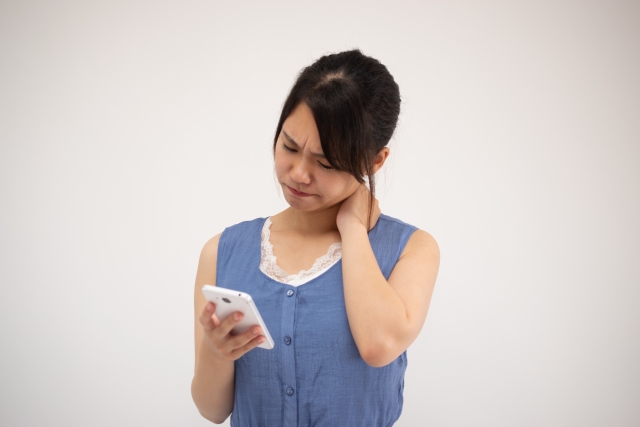 スマホをもって首の痛みを訴える女性